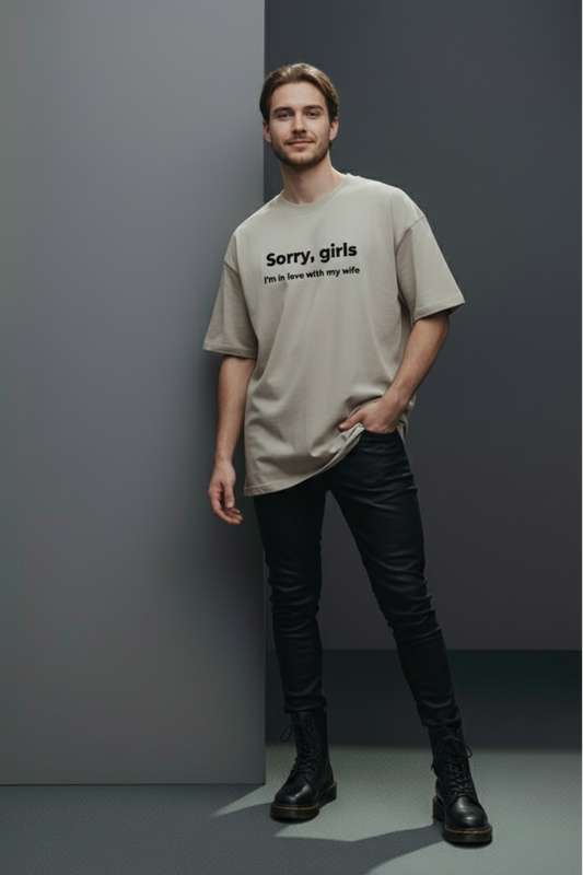 Man wearing a beige t-shirt with text, black pants, and boots against a gray background